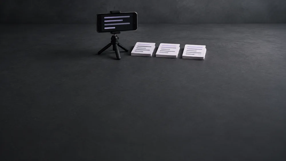 Landscape phone on a tabletop tripod beside three separate stacks of script cue cards.
