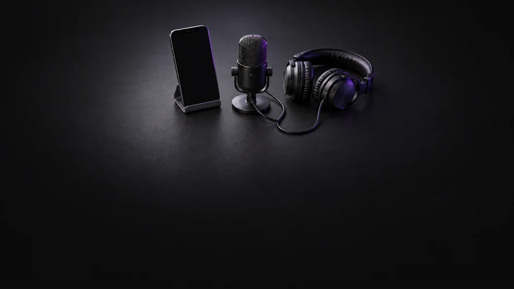 Unbranded phone beside a microphone and headphones on a dark desk.